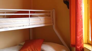 Una cama litera con estructura blanca y almohada roja, una ventana con cortinas rojas y un radiador en la pared.