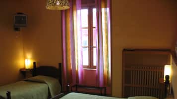 Ein Zimmer mit zwei Einzelbetten, einem kleinen Tisch, einem an der Wand montierten Fernseher und einem Fenster mit Vorhängen.