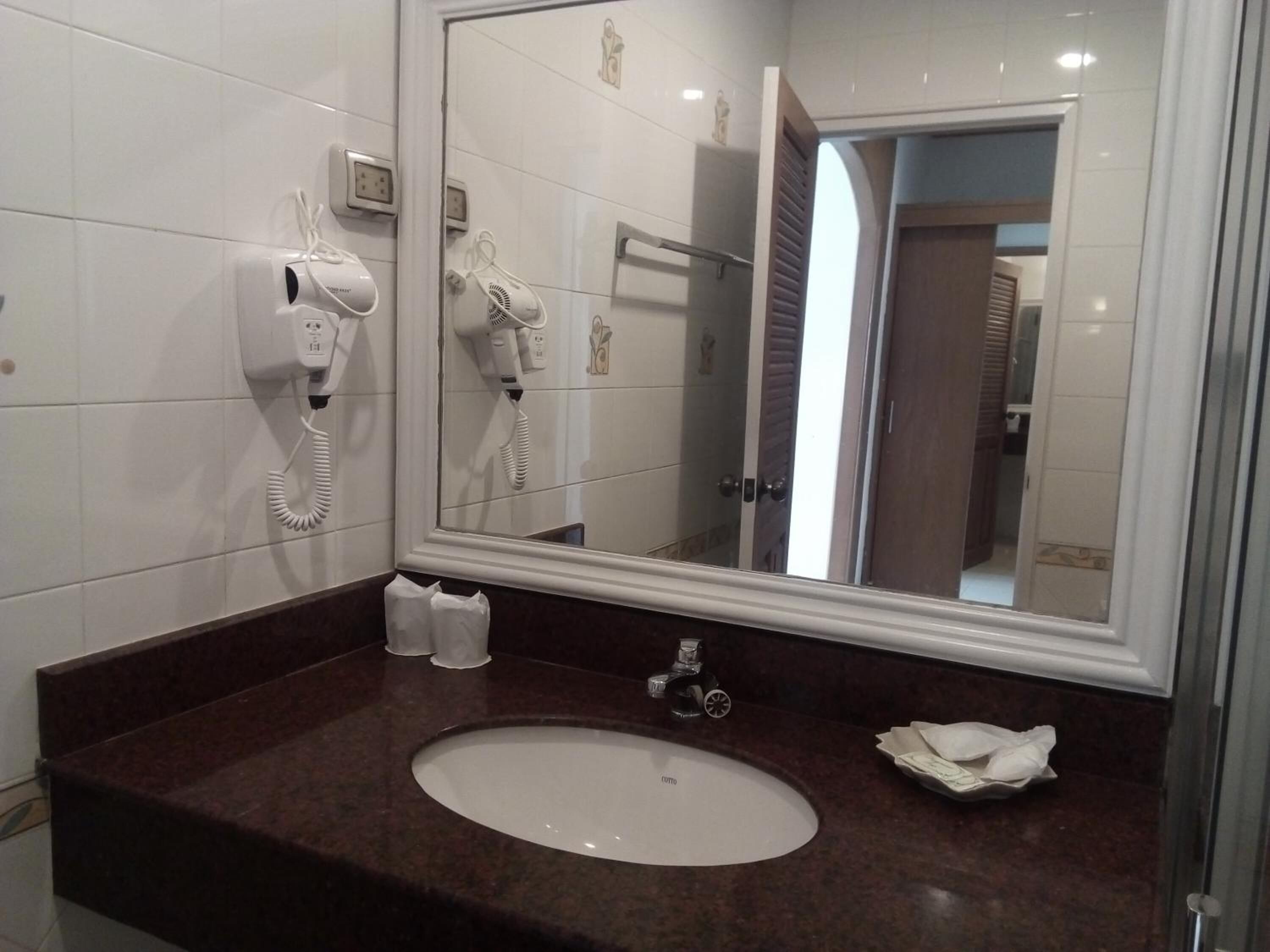 A bathroom with a white sink, a mirror, a hairdryer, and a towel dispenser.
