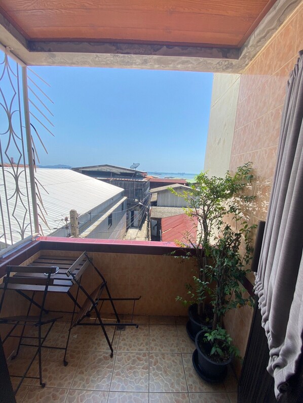 Un balcón con vista al mar, una silla de metal y plantas en macetas.