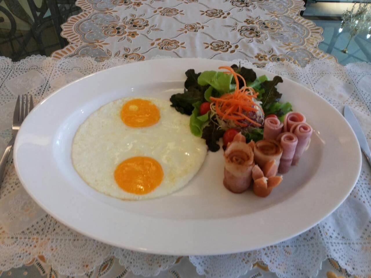 Une assiette avec deux œufs au plat, une salade en accompagnement et des tranches de jambon roulées.