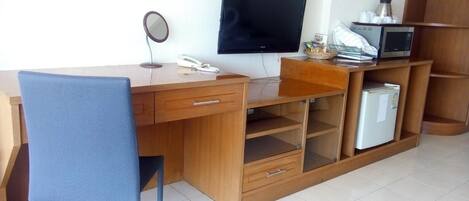 A compact office space with a wooden desk, a chair, a television, a telephone, and a small refrigerator.