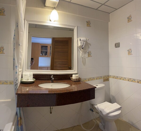 A bathroom with a sink, mirror, toilet, and a hairdryer on the wall. - Seaview Sriracha Hotel (Si Racha)