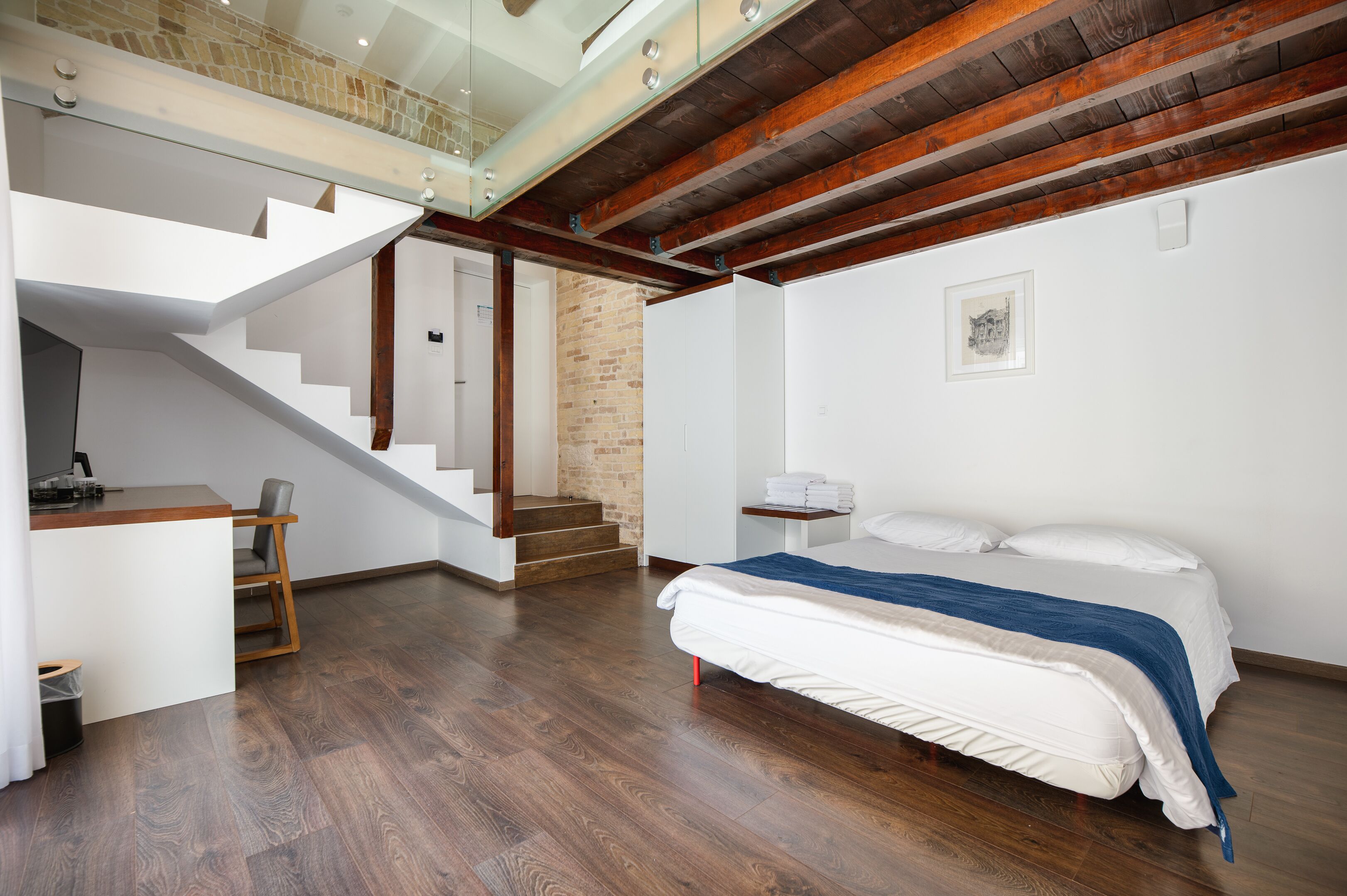 A modern bedroom with a large bed, a desk, and a staircase leading to an upper level.