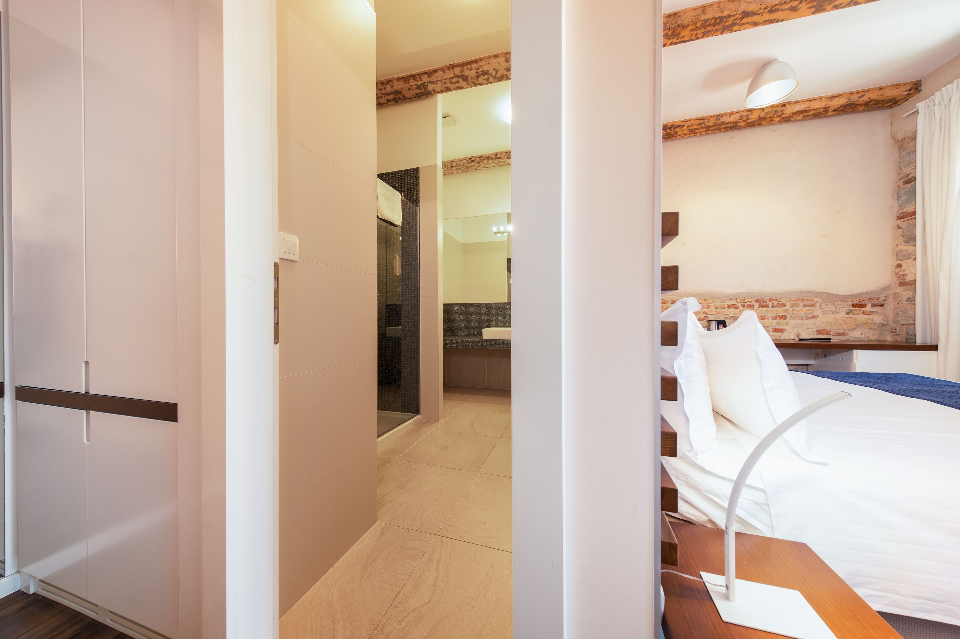 Ein Hotelzimmer mit Bett, Nachttisch, Lampe und Blick auf das Badezimmer und den Flur.