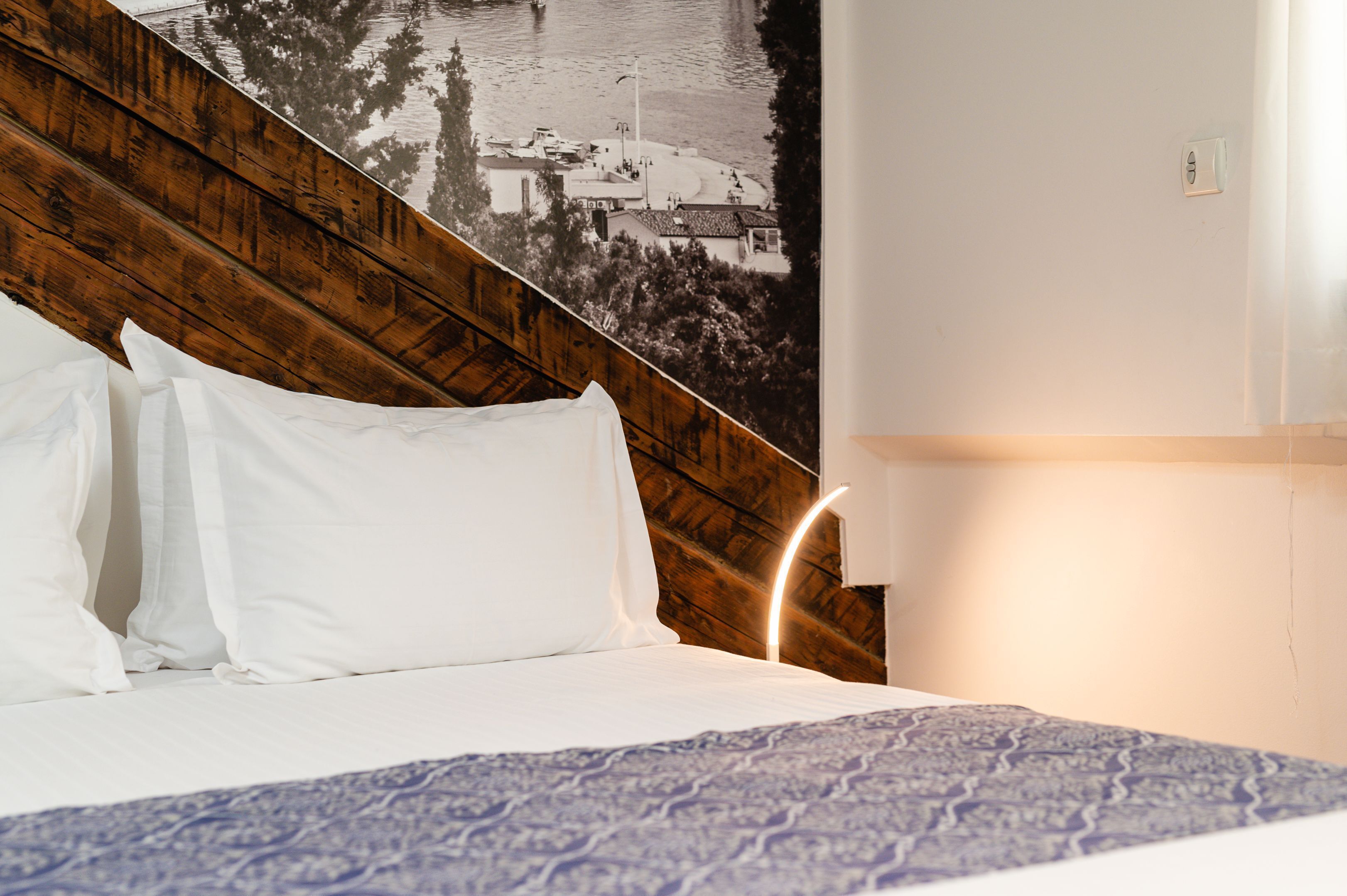 A bed with white pillows and a patterned bedspread, a wooden headboard, and a wall-mounted light fixture.