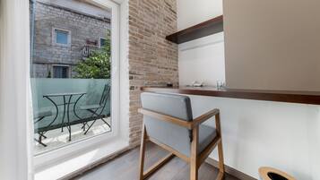 Uma cozinha compacta com bancada de madeira, uma cadeira e janela com vista para uma varanda com mesa e cadeiras.