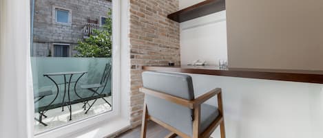 Una cocina pequeña con encimera de madera, una silla y un ventanal con vistas a un balcón que tiene una mesa y sillas.