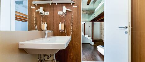 A modern bathroom with a wooden wall, a white sink, and a hairdryer mounted on the wall.