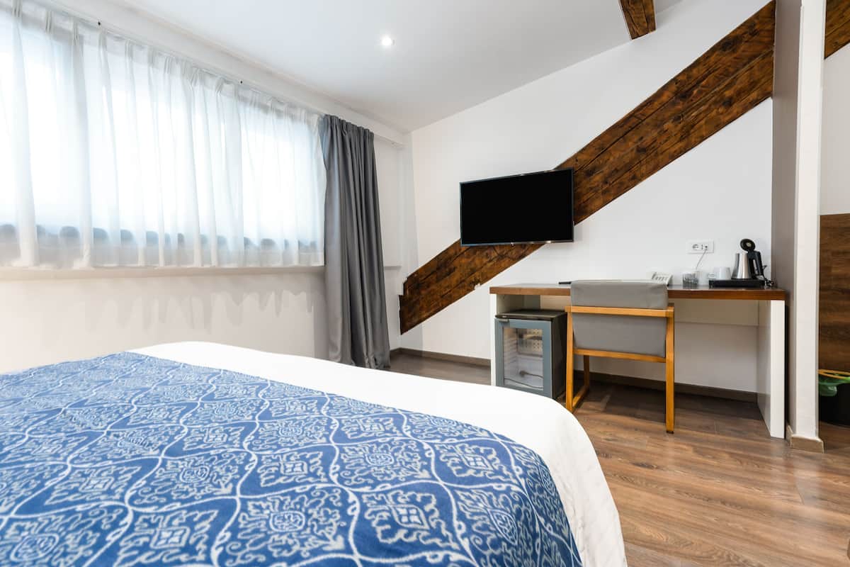 Un dormitorio con una cama grande, un escritorio, una silla y un televisor montado en la pared.