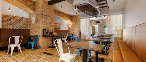 A spacious restaurant with brick walls, wooden beams, and a mix of white and blue chairs.