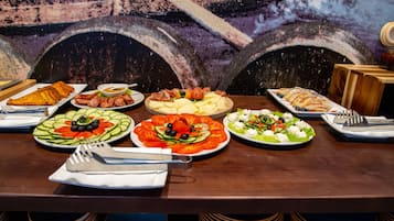 Une table dressée avec divers plats, notamment des salades, des viandes et des pâtisseries, le tout mis en valeur par une fresque murale en arrière-plan.