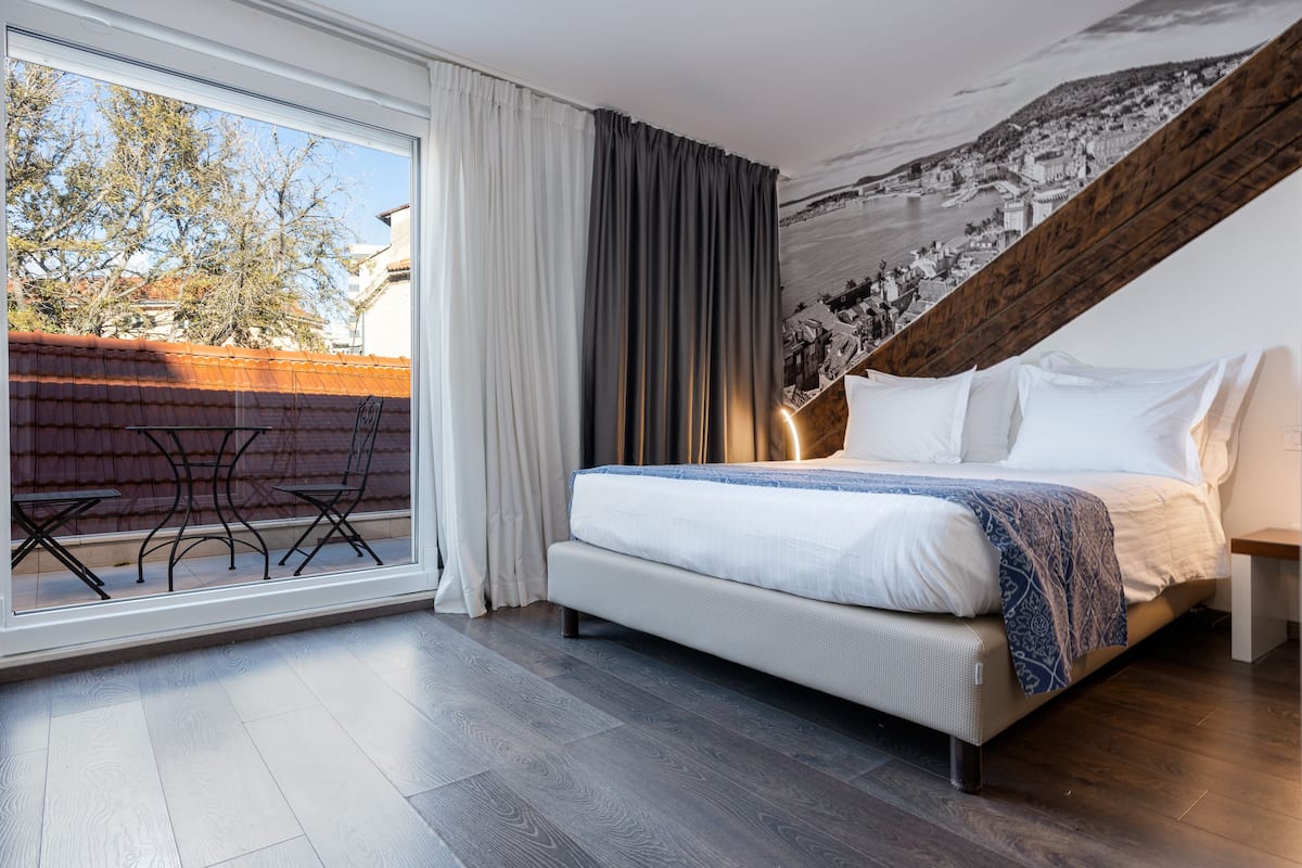 Un dormitorio con cama, ventana con cortinas, vista al exterior y un mural en la pared.