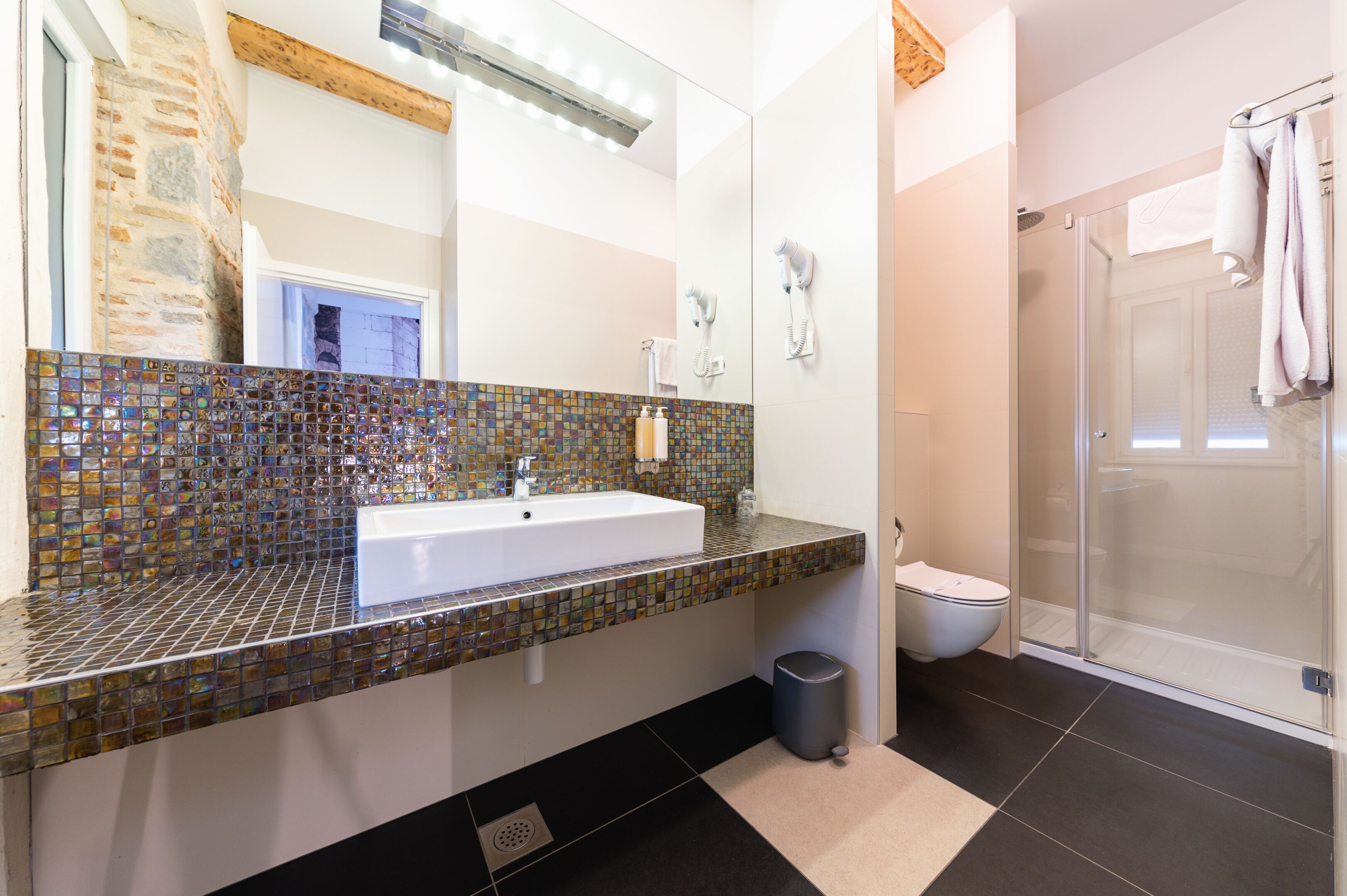 A bathroom with a mosaic tile backsplash, a white sink, a glass shower enclosure, and a toilet.