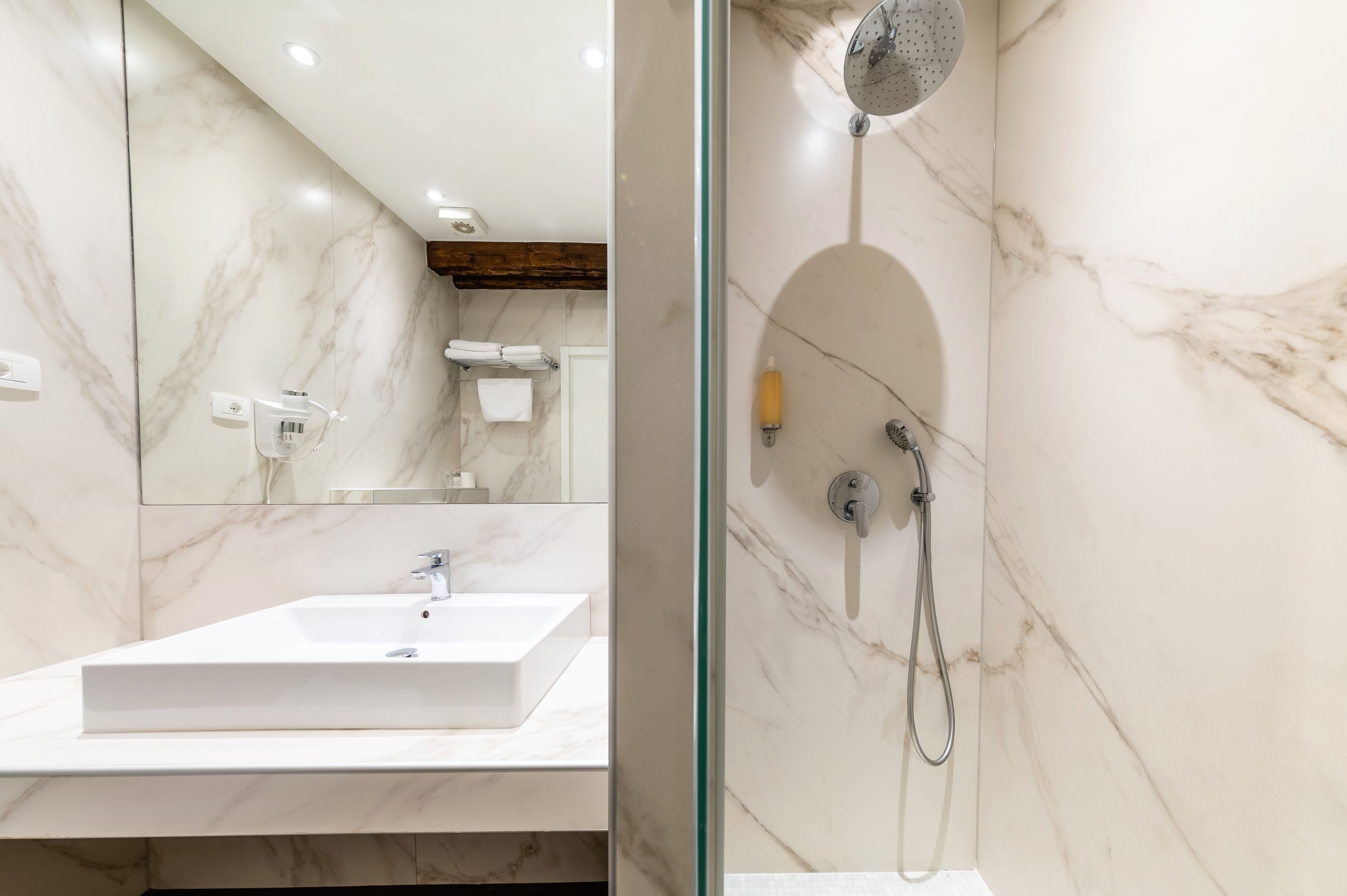 A modern bathroom with a marble sink, a glass-enclosed shower, and a wooden beam ceiling.