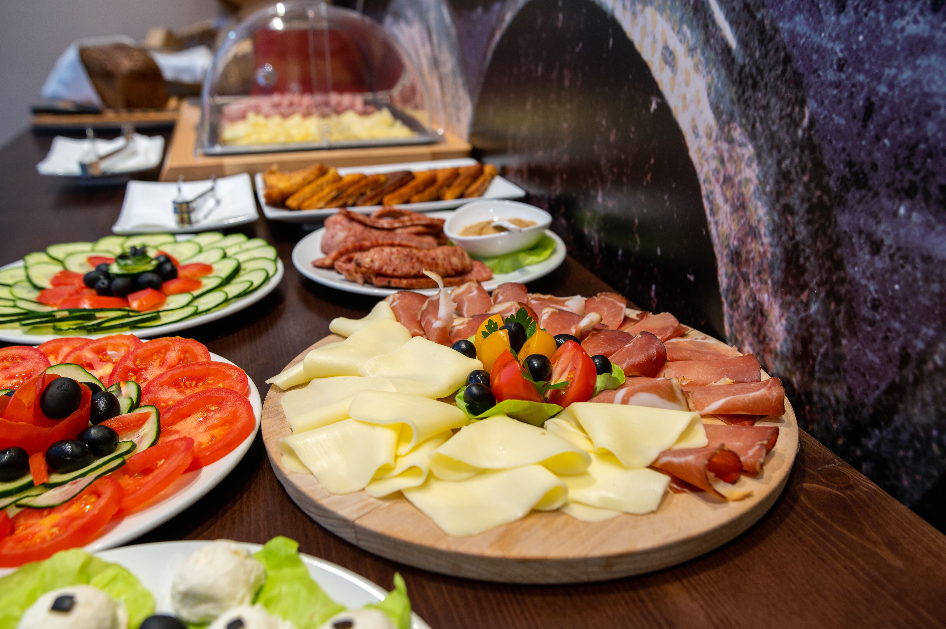 Une variété d’aliments sont disposés sur une table, notamment des tomates en tranches, du fromage, des olives et de la charcuterie.