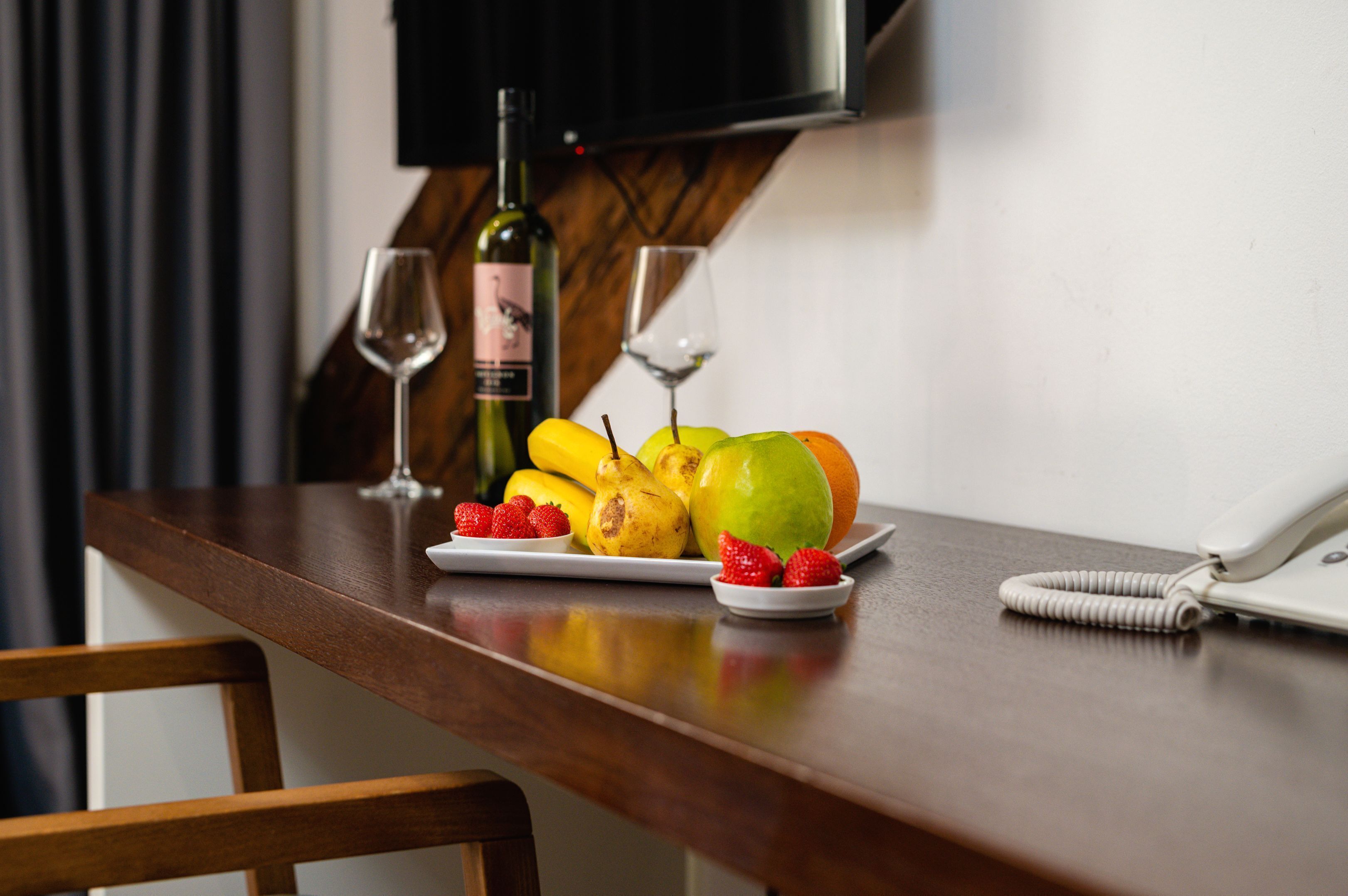 Una mesa de madera con un plato de fruta, una botella de vino y dos copas de vino.