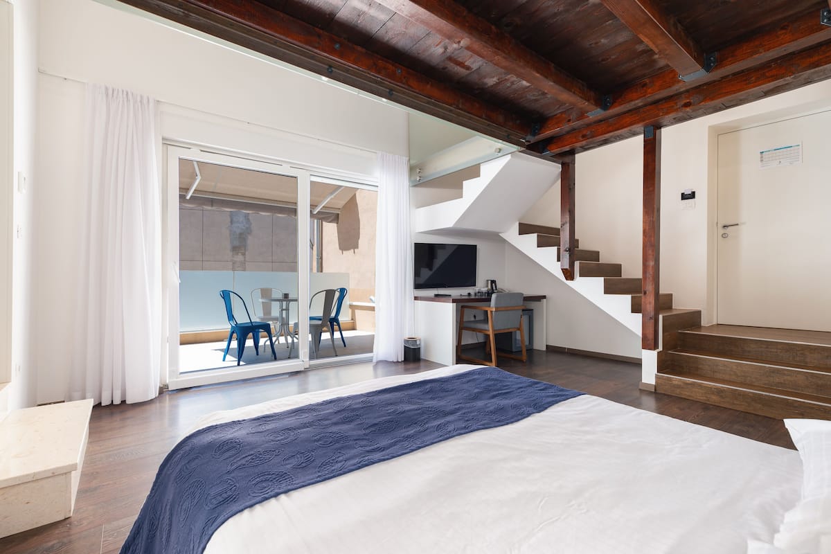 Habitación de hotel con cama, escritorio, silla, televisión y escalera.