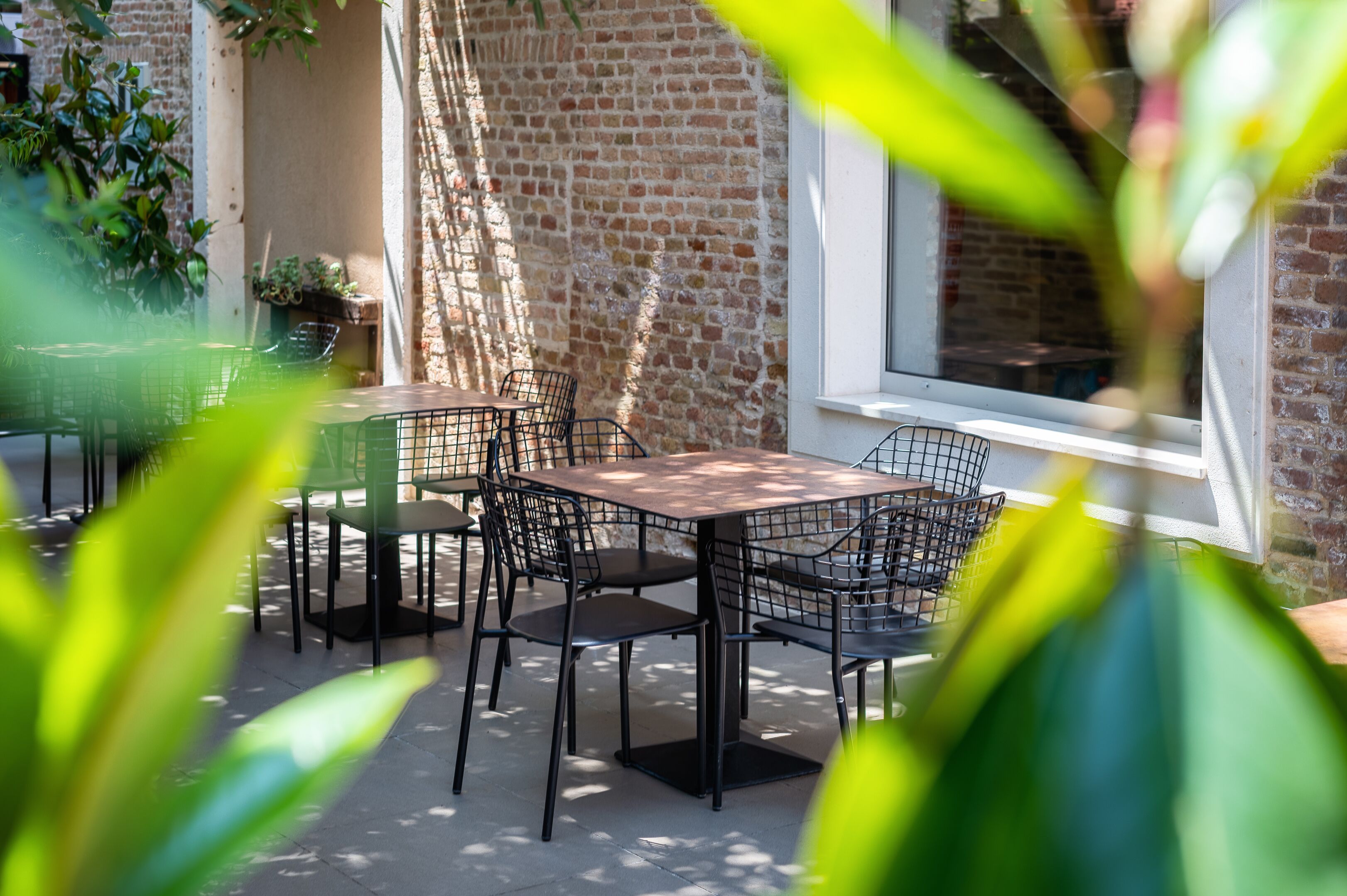 Een terras buiten met een bakstenen muur, een tafel met stoelen en potplanten.