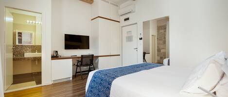 A hotel room with a bed, a desk with a chair, a television, and an air conditioning unit.