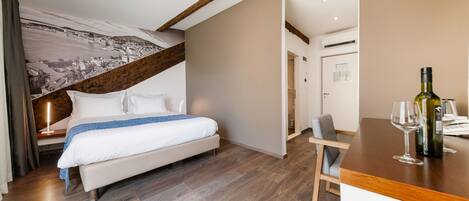 A modern hotel room with a bed, wooden flooring, a desk with a wine bottle and glass, and a large wall mural.