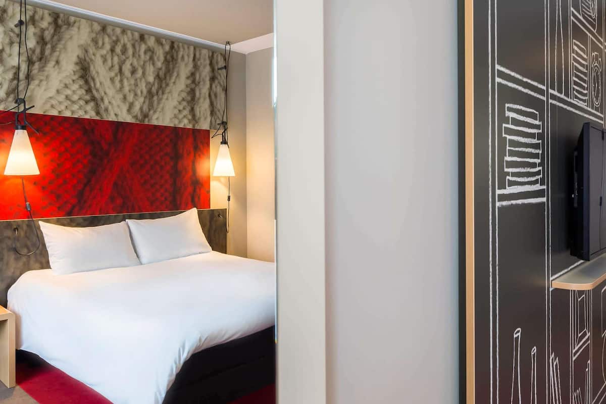 A hotel room with a bed, two bedside lamps, a TV, and a red carpet.