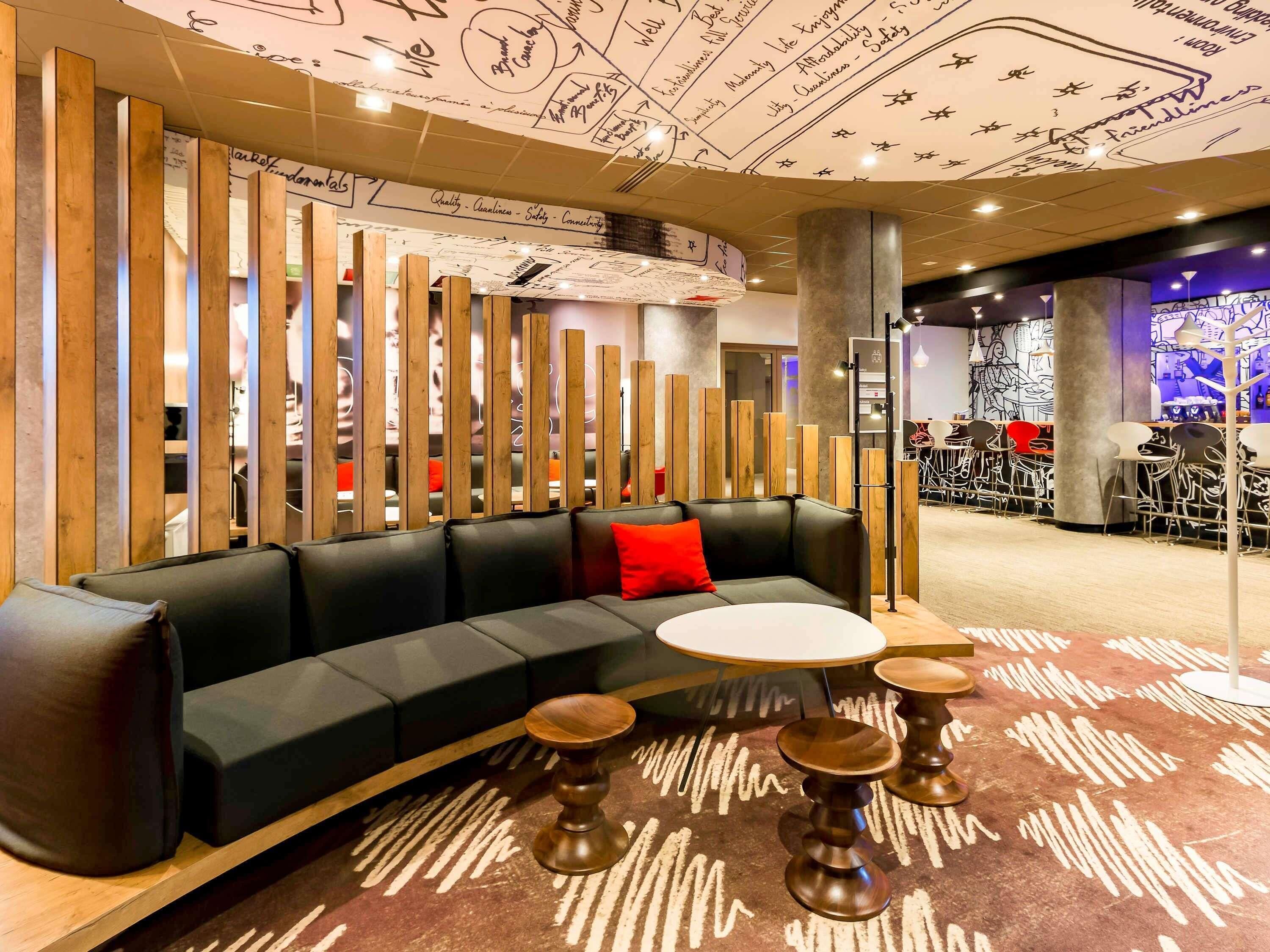 Un espace détente moderne avec un canapé en cuir noir, une table ronde en bois et un tapis à motifs.