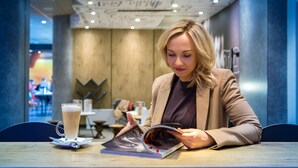 Une personne assise à une table, avec une boisson et un magazine.