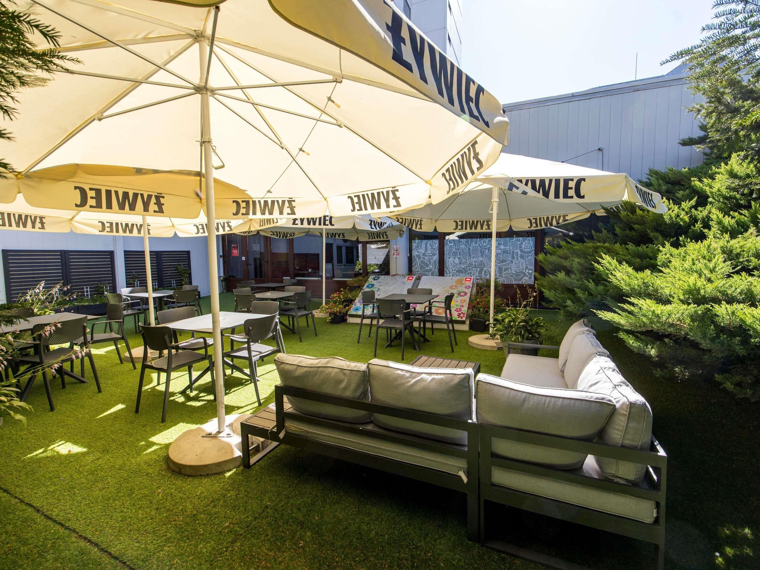 An outdoor seating area with tables and chairs under large umbrellas, a sofa, and artificial grass.