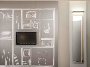 A modern room with a flat-screen TV mounted on a chalkboard wall, a mirror, and a door with a light above it. - ibis Wroclaw Centrum (Wroclaw)