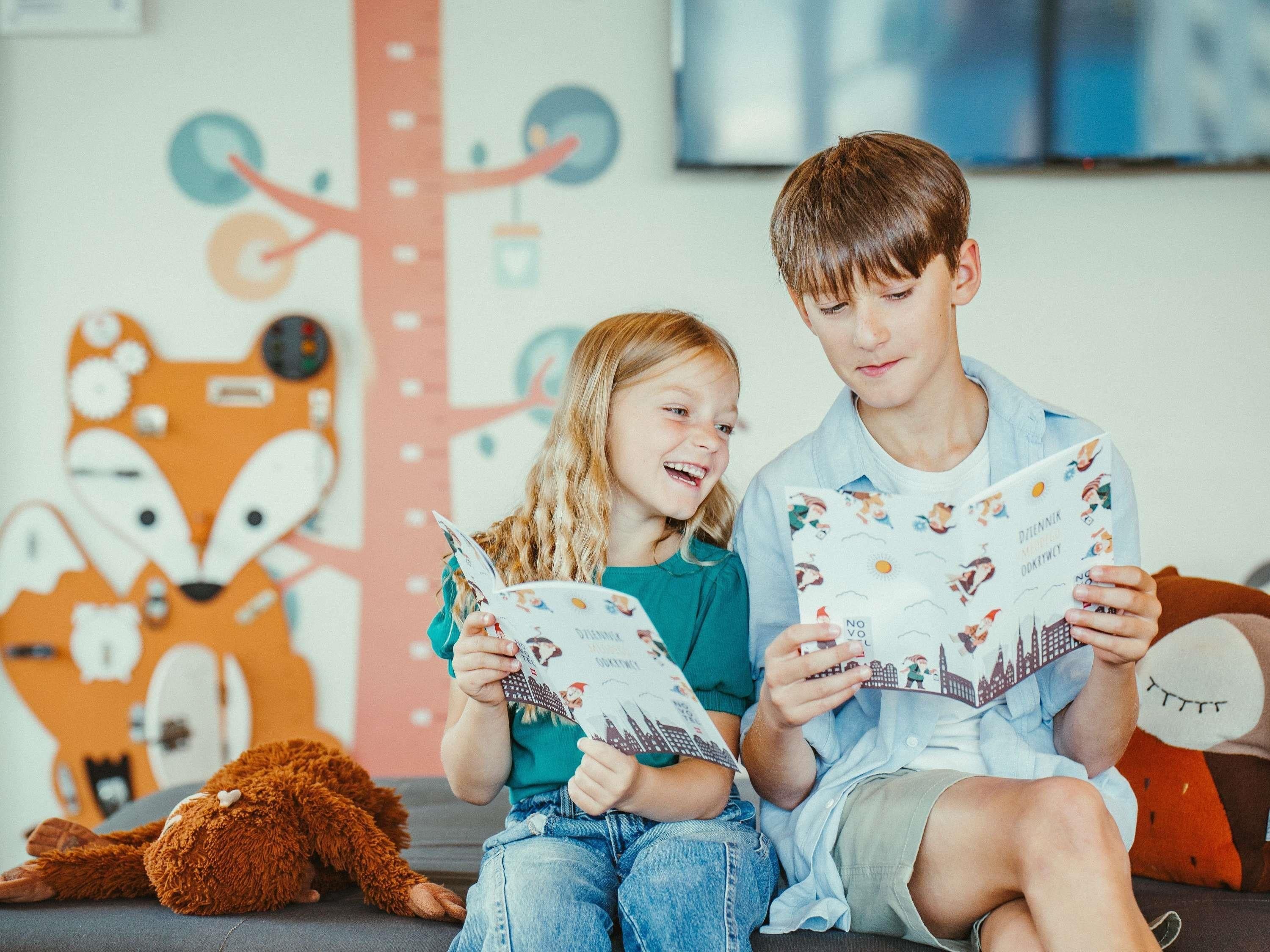 Two children sitting on a couch, reading books.