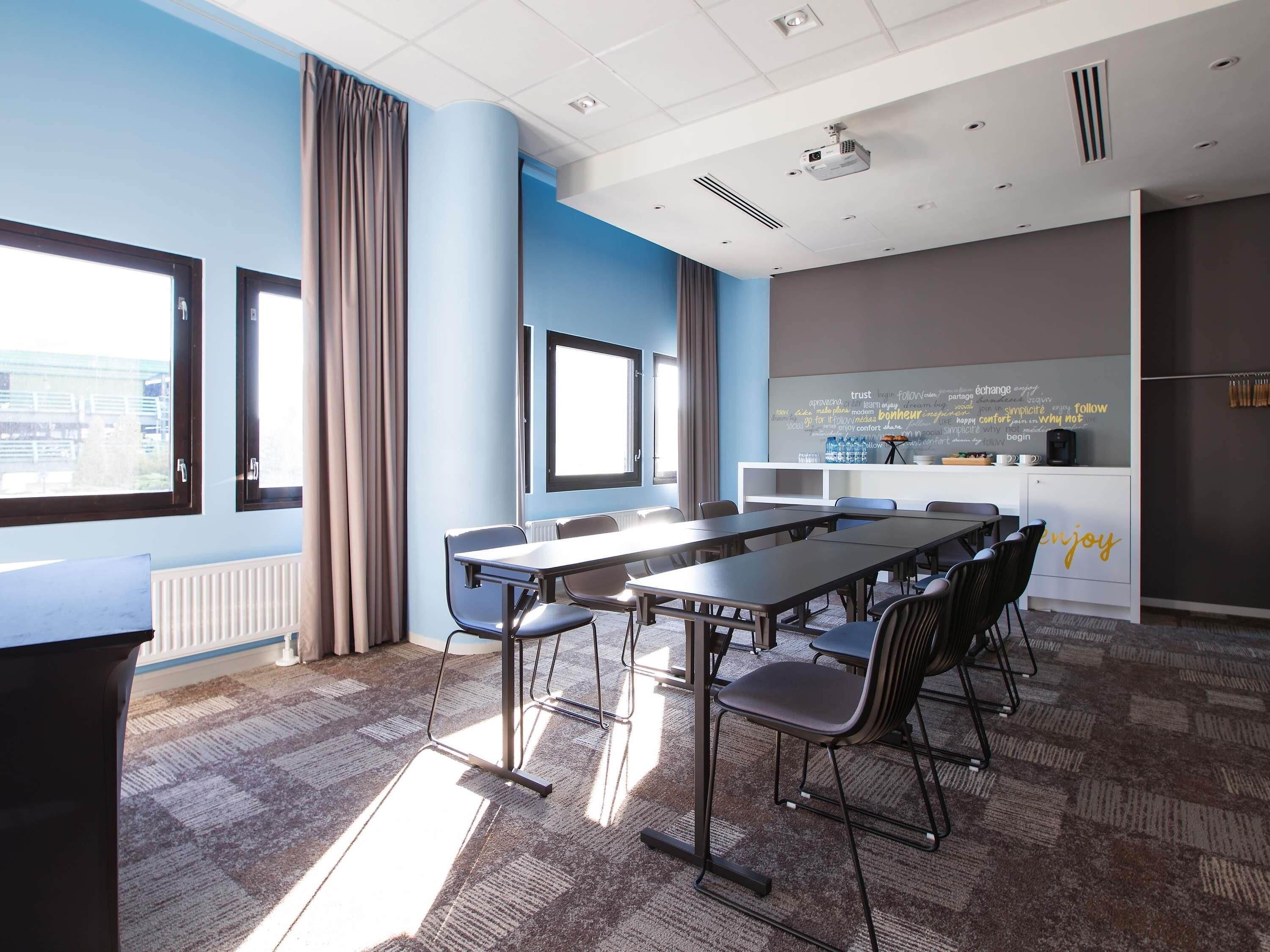 A modern conference room with a long table, chairs, a projector, and a word cloud on the wall.
