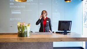 A hotel reception desk with a computer monitor, a vase of flowers, and a wall displaying room rates and services. - ibis Wroclaw Centrum (Wroclaw)