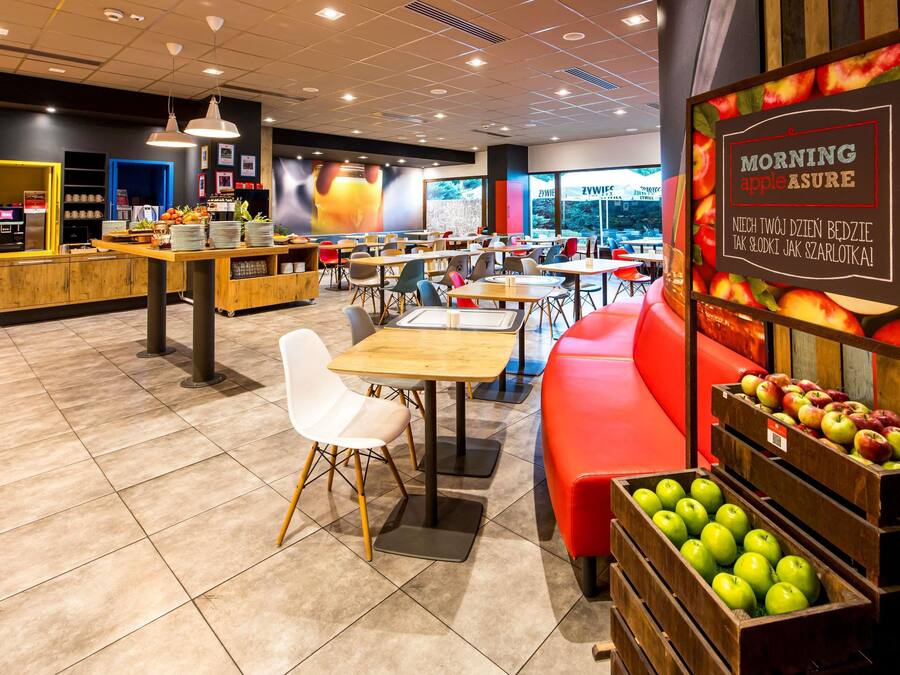 Interior moderno de una cafetería con mesas, sillas y una exhibición de frutas.
