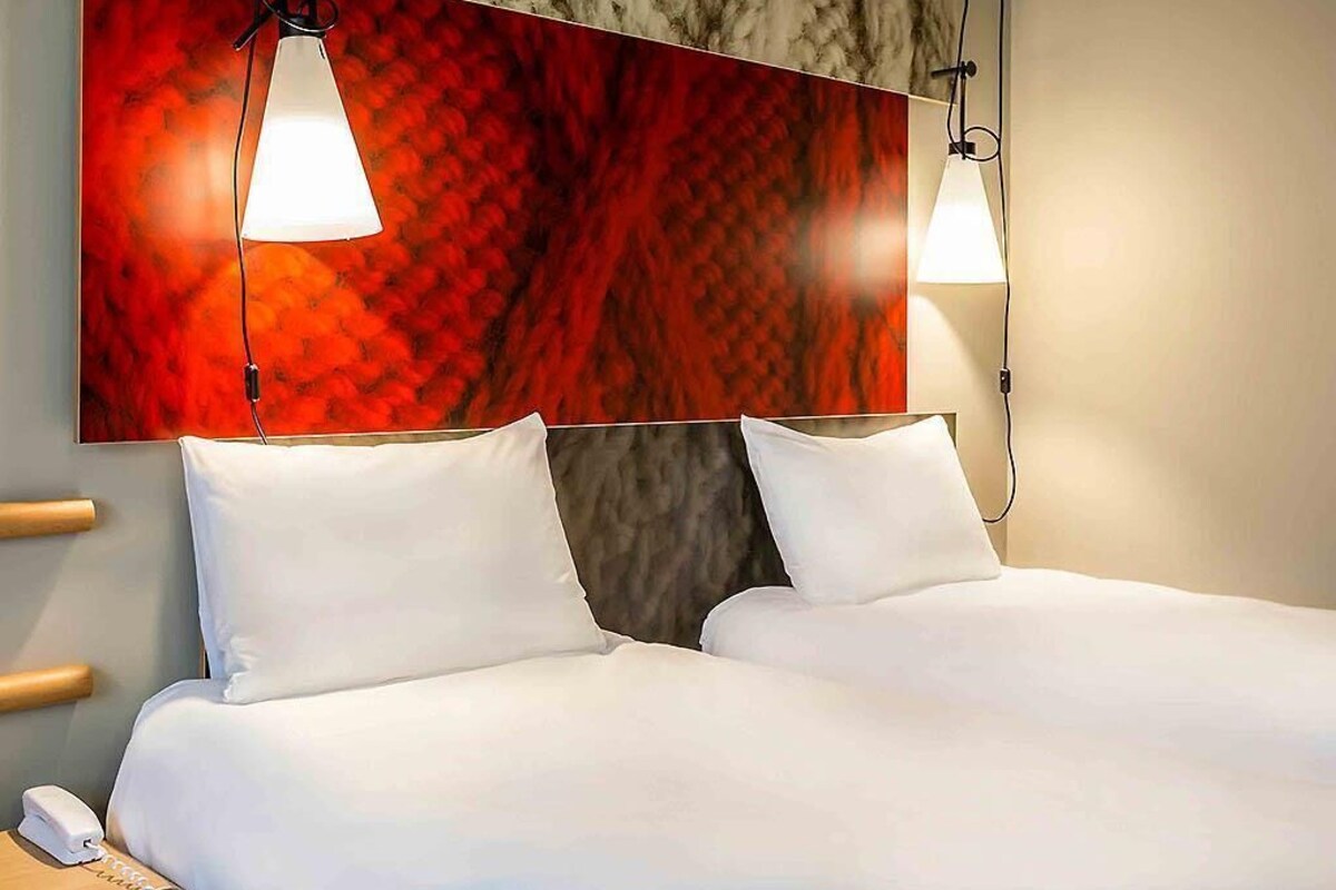 A hotel room with a bed, white pillows, a telephone, and two pendant lights.