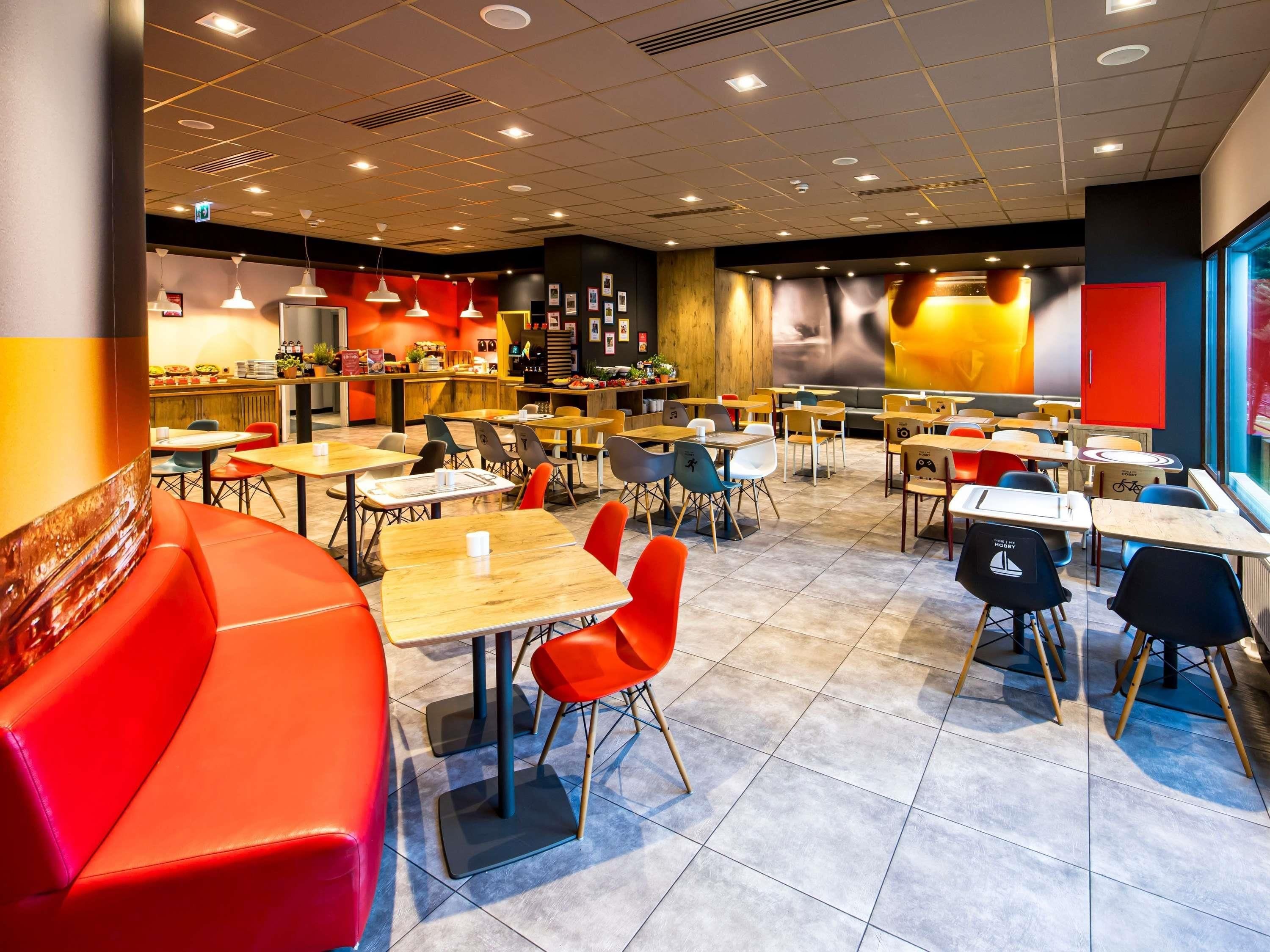 Un restaurant doté de plusieurs tables et chaises, d’un comptoir et d’un espace salon avec un canapé rouge.