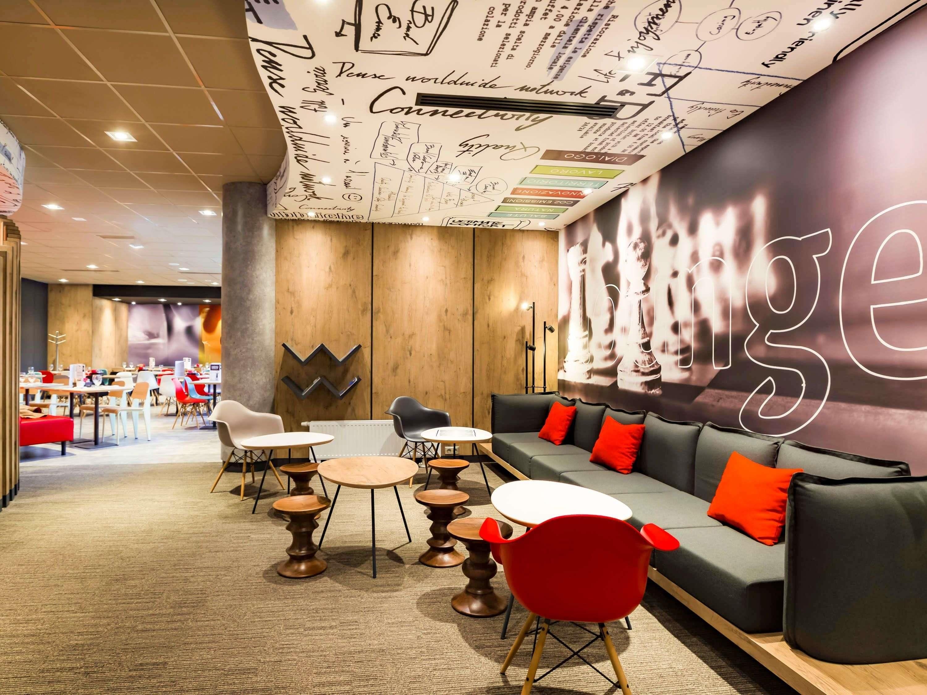 Un área de estar moderna con un gran mural, disposiciones de asientos y una cocina visible al fondo.