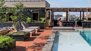 Un área de piscina en la azotea con sillones de descanso, un bar y vistas a la ciudad.