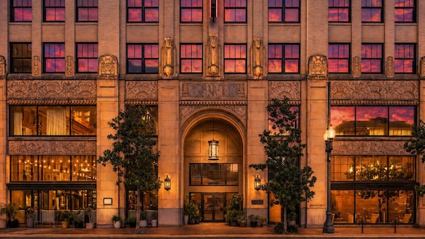 Fachada imponente y ornamentada de un hotel, con múltiples ventanas, una entrada arqueada central e iluminación decorativa.