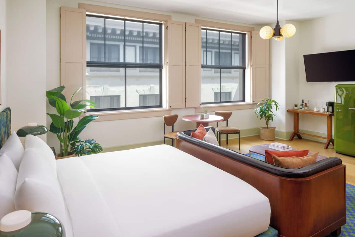 A hotel room with a large bed, a seating area with a table, and a TV on the wall.