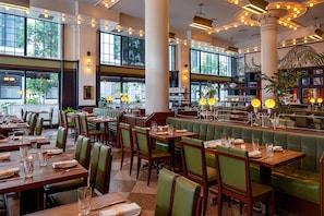 A restaurant with multiple dining tables and booths, large windows, and decorative lighting. - The Barnett - JDV by Hyatt (New Orleans)