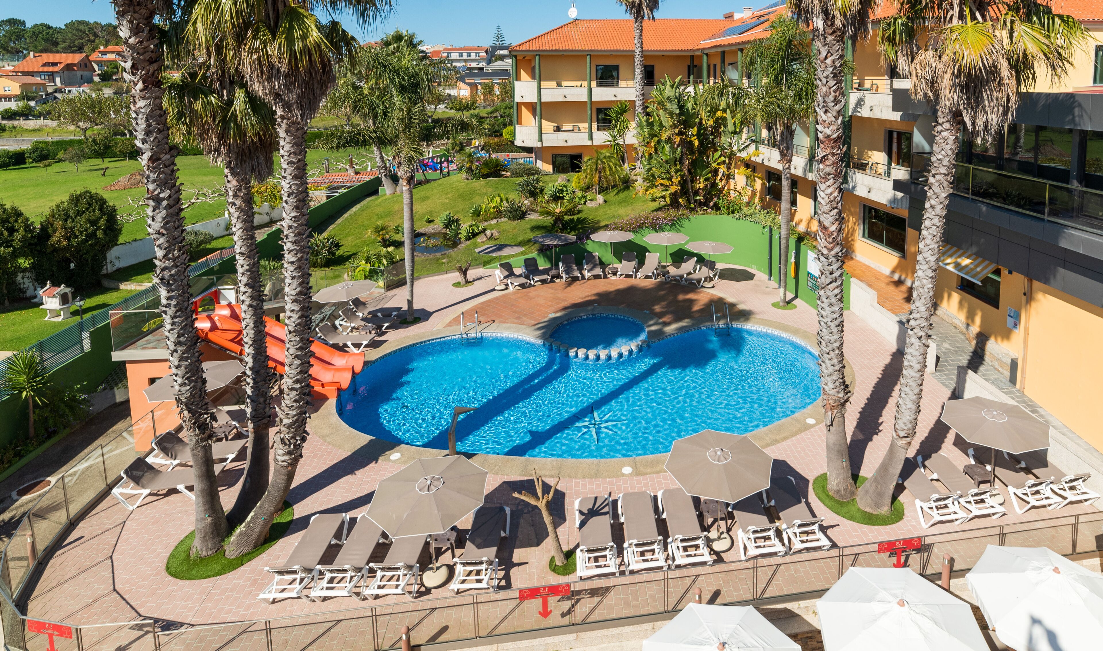 Un área de piscina con dos piscinas, sillas de descanso, sombrillas y palmeras.