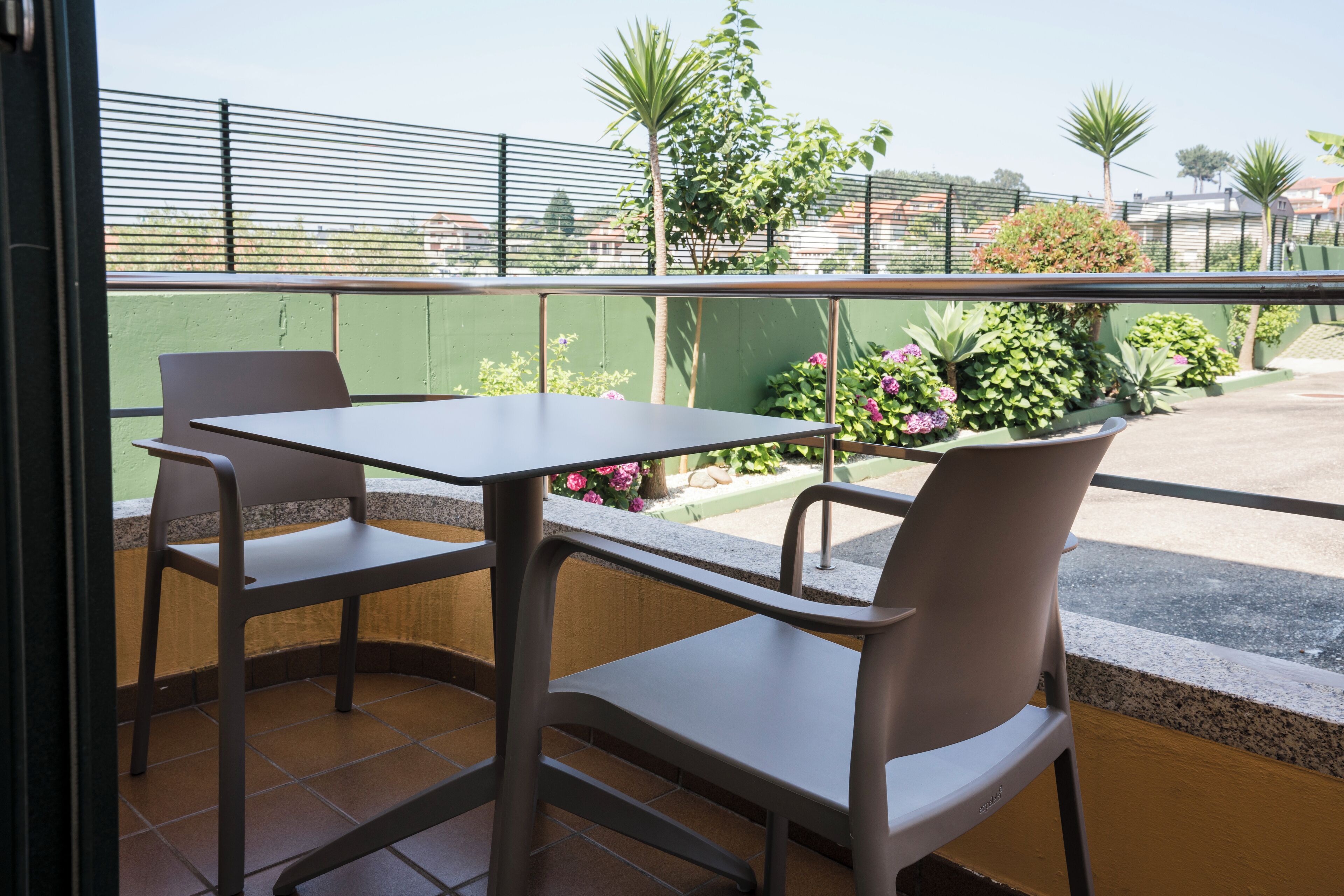Un balcon avec deux chaises et une table, donnant sur un jardin où poussent différentes plantes et fleurs.