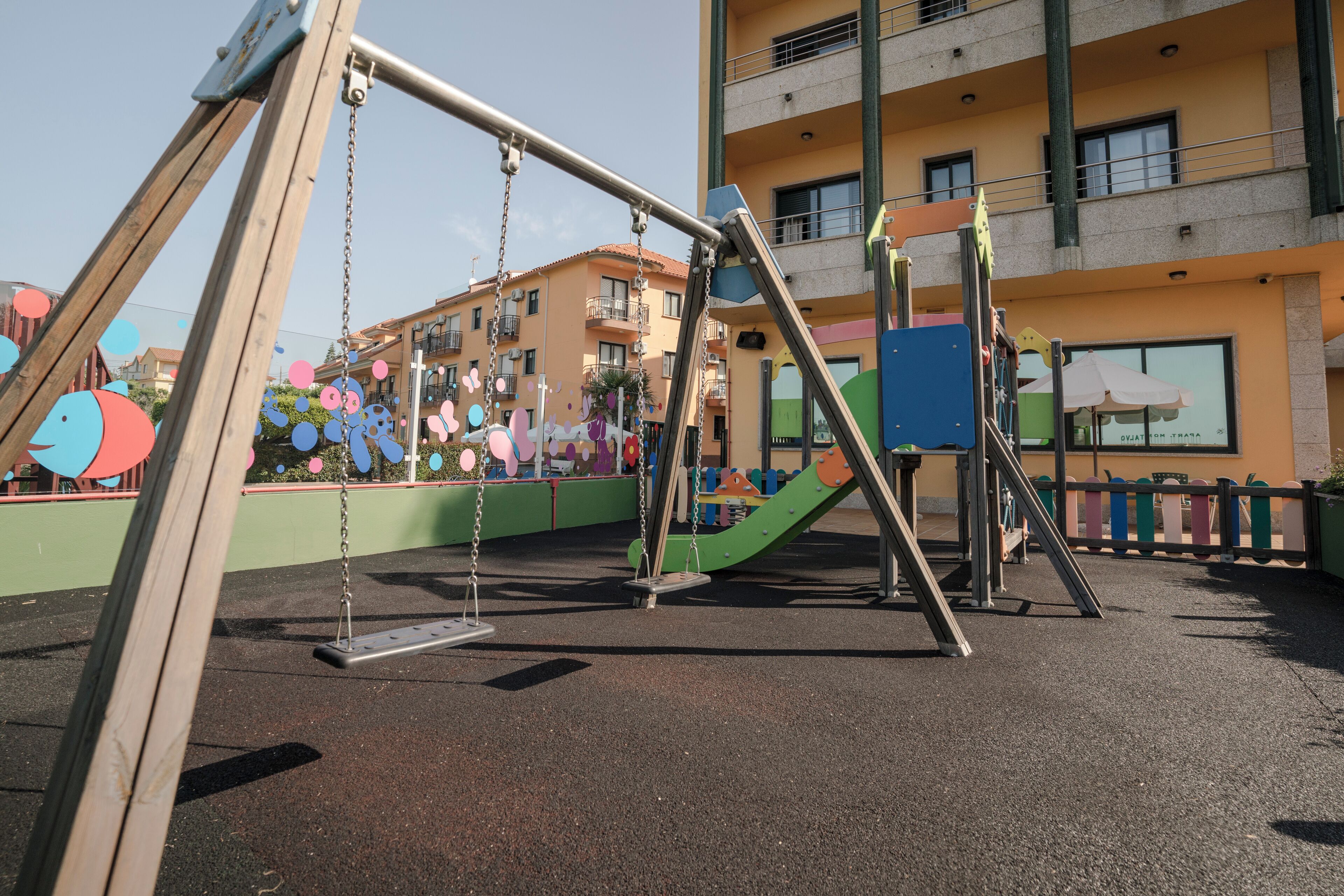 A playground with swings and slides, surrounded by a multi-story building with balconies.