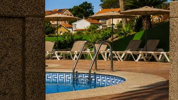 Zona de piscina con sillas de descanso, piscina con mosaicos azules y palmeras.