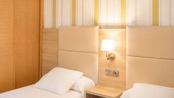 Une chambre d’hôtel avec deux lits simples, une armoire en bois et un motif rayé sur le mur.