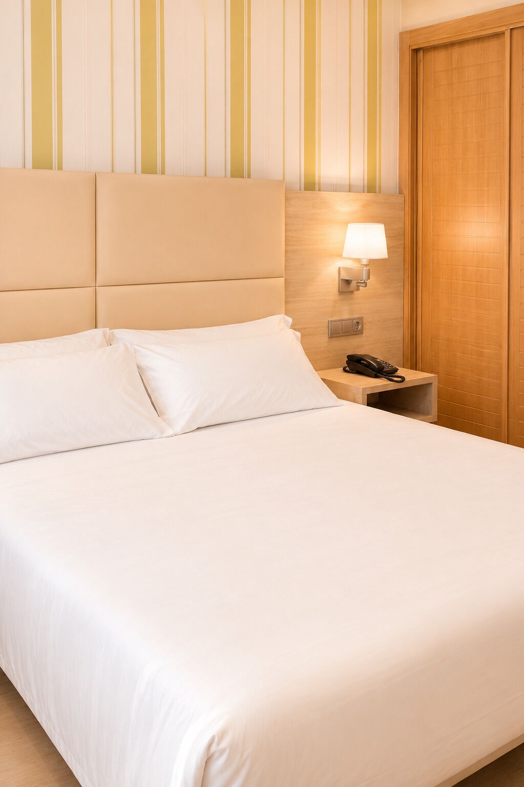 Habitación de hotel con una cama, una lámpara de noche, un teléfono y una puerta de madera.