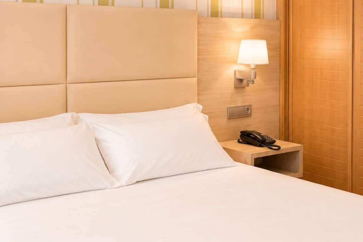 A hotel room with a bed, a bedside lamp, a phone, and a wooden door.