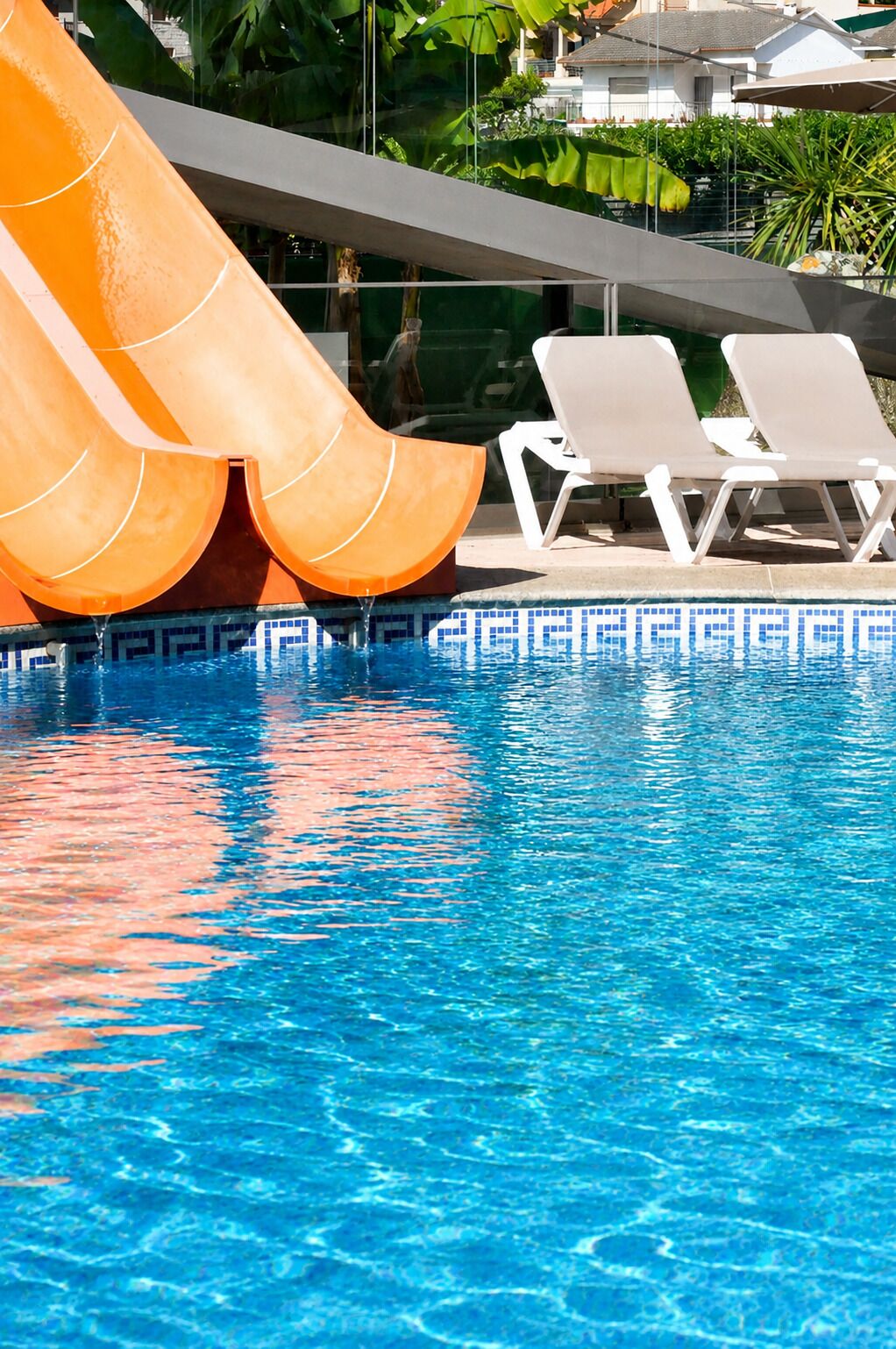 A swimming pool with a water slide, lounge chairs, and a tiled edge.