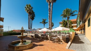 An outdoor patio area with a fountain, seating, and palm trees.